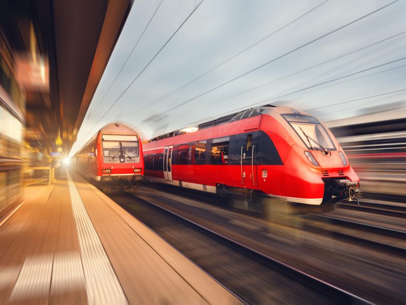 Modern high speed red passenger trains at sunset. Railway station in Nuremberg, Germany. Railroad with motion blur effect. Industrial concept landscape
